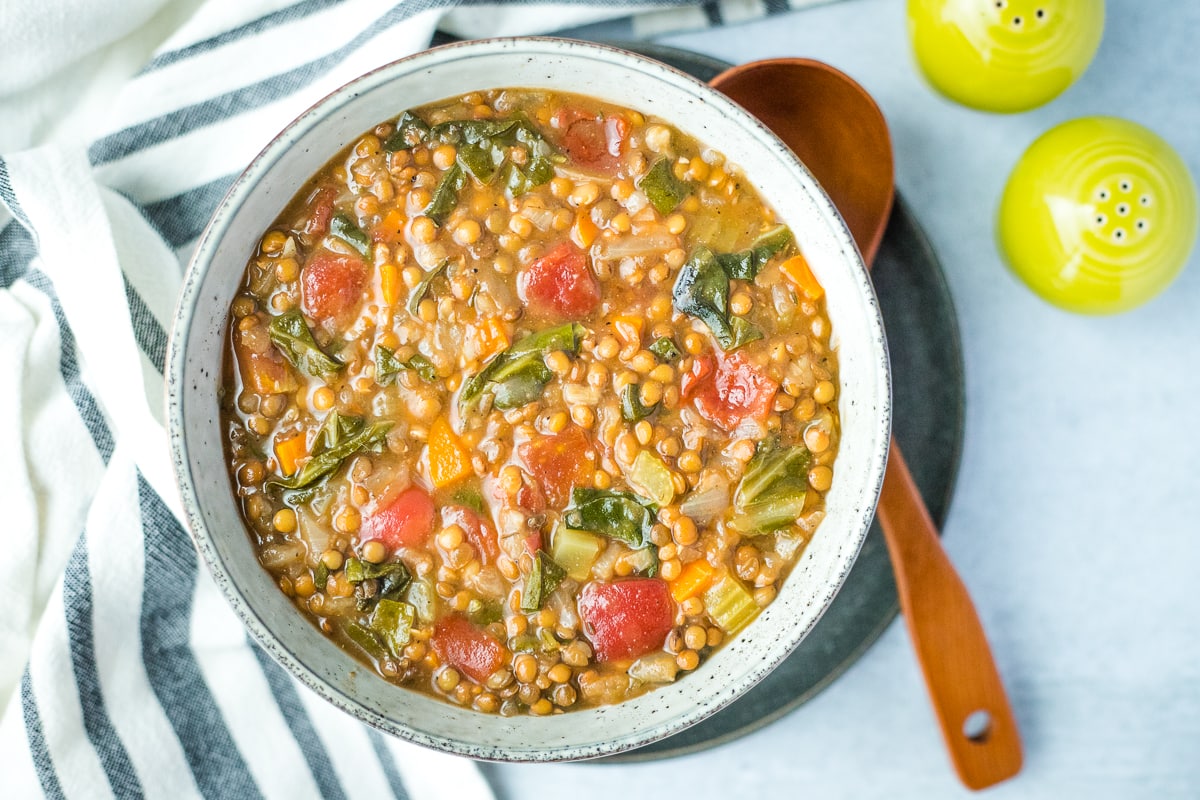 bowl of cooked lentil soup with brown wood spoon