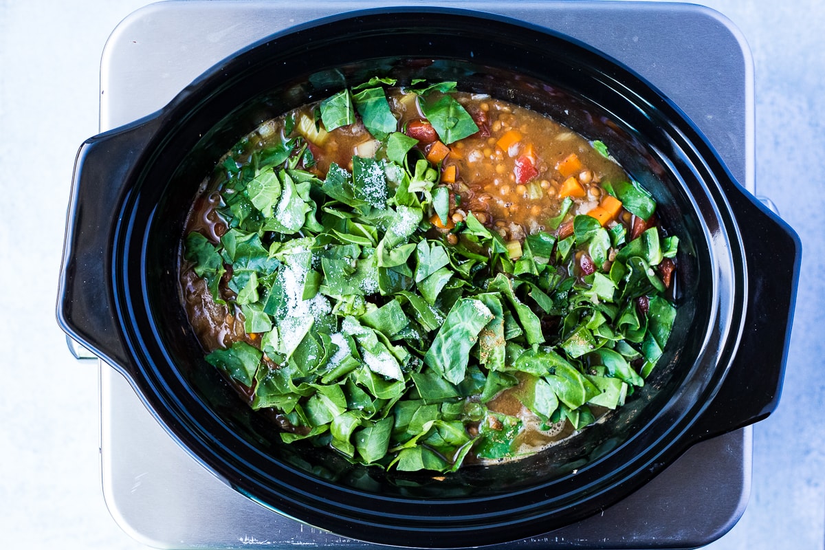 adding chopped swiss chard to soup in a slow cooker