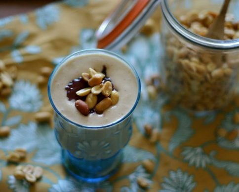 blue glass with peanut butter smoothie topped with strawberry jam and chopped peanuts