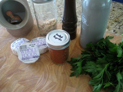 ingredients to make cana de cabra. salt in a ceramic salt hog, rounds of cheese, mas jar of sliced almonds, small mason jar of smoked paprika, pepper mil, fresh parsley and large bottle of olive oil