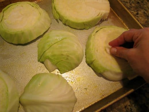 Rubbing sliced cabbage steaks with raw garlic clove on a baking sheet