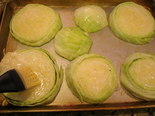 Using a silicone pastry brush to rub olive oil all over the cabbage steaks on a baking sheet
