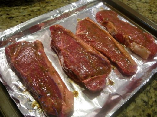 uncooked strip steaks on a tin-foil lined baking sheet