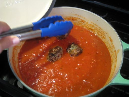 putting pesto meatballs into sauce with tongs