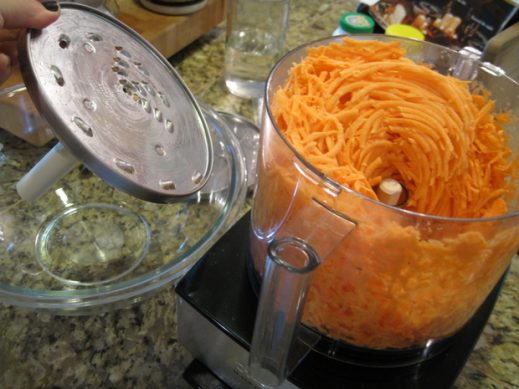 food processor bowl fitted with shredding blade and showing shredded sweet potatoes for sweet potato latkes