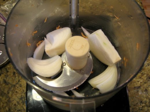 bowl of food processor fitted with chopping blade about to chop quartered sweet onion for sweet potato latkes