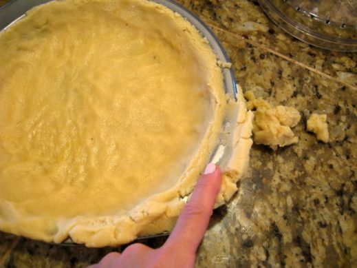 pressing paleo pie crust dough into pie pan and removing excess dough from sides