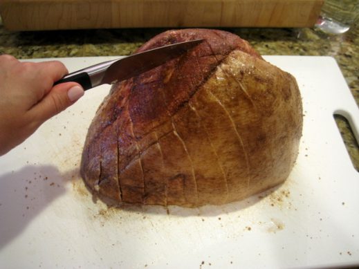 using a paring knife to cut diagonal slices into a smoked ham before going into the oven