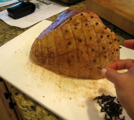 placing whole cloves into a whole ham before going into the oven