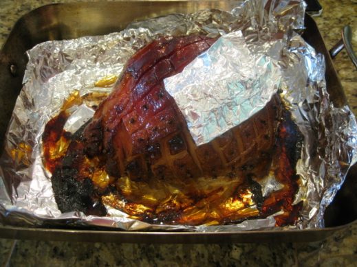 cooked whole smoked spiced ham covered with small pieces of tinfoil while resting