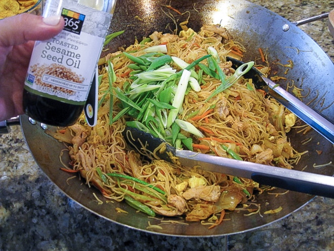 putting sesame oil and scallions on singapore rice noodles right before serving