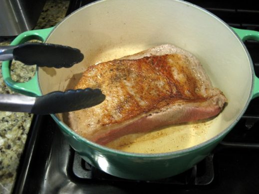 using tongs to turn brisket in a dutch oven on the stove for passover