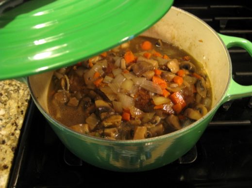 placing a lid on beef brisket and vegetables in broth to go into the oven to finish cooking