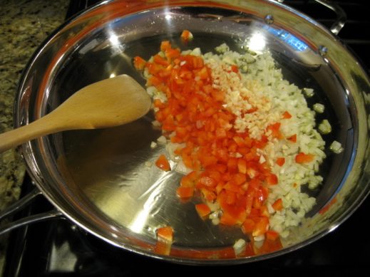 large frying pan with oil, chopped garlic, onion and red pepper