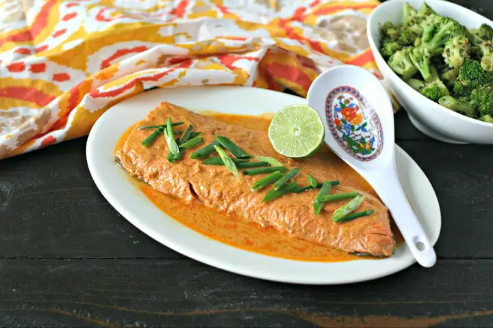 platter of cooked wild salmon with red curry sauce, lime and sliced scallions