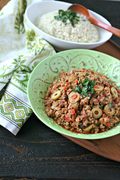 cooked chicken picadillo in a green bowl in front of a white bowl of cauliflower rice