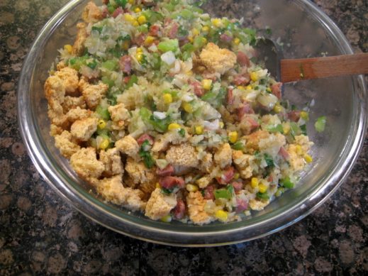 large mixing bowl with ingredients to make cornbread sausage stuffing getting mixed by a wooden spoon