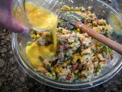 large glass mixing bowl. adding beaten eggs to cornbread sausage stuffing mixture