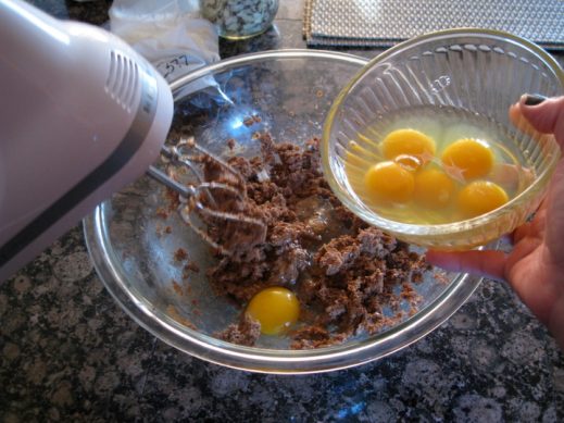 adding eggs one at a time to glass bowl with sugar and butter