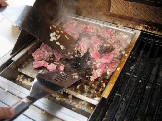 cooking Philly cheese steak meat and onions on a griddle