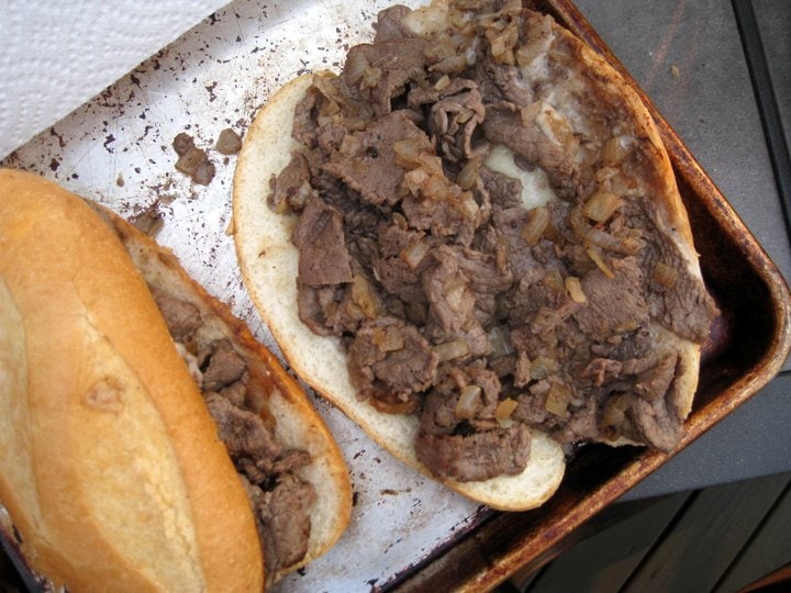 open face hoagie roll with philly cheese steak meat on a baking sheet