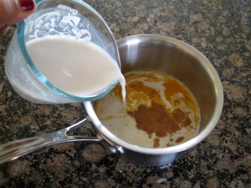 pouring cashew milk and spices into a pot for turmeric milk