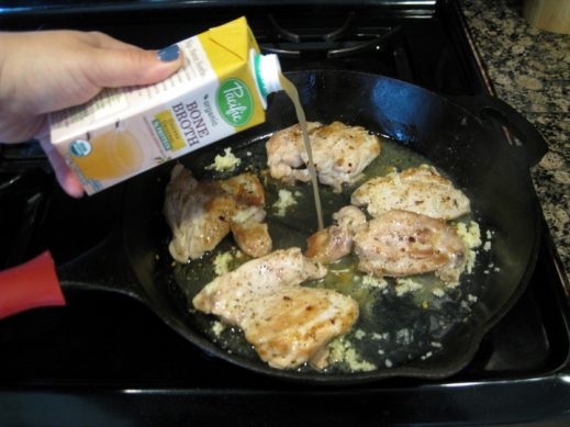 pouring Pacific Foods Chicken Bone Broth over chicken thighs in a cast iron pan