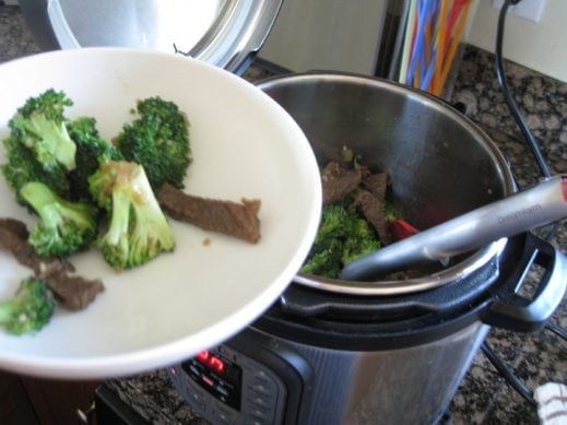 removing beef and broccoli with tongs to a white serving plate