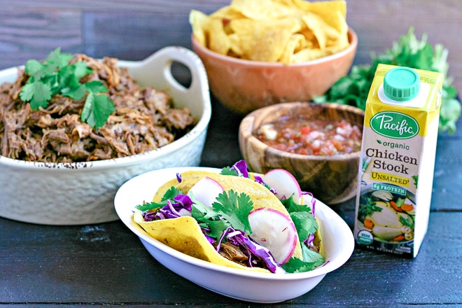 pulled pork tacos in front of bowl of instant pot pulled pork, salsa, broth and chips