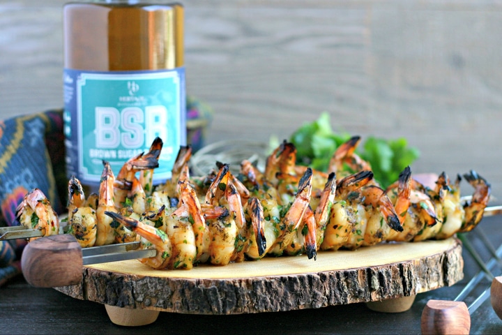wood serving platter with shrimp skewers on top and bottle of bourbon in background