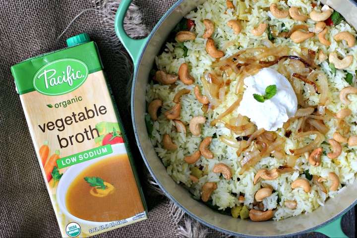 cooked vegetable biryani in a large pot and a carton of vegetable broth