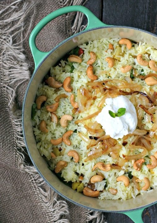 cooked vegetable biryani in a large pot topped with cashews and yogurt