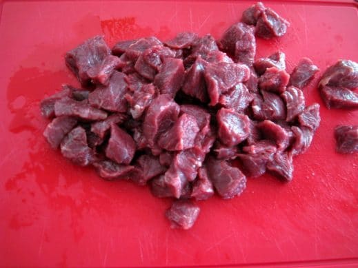 beef stew meat on a red cutting board cut into bite sized pieces