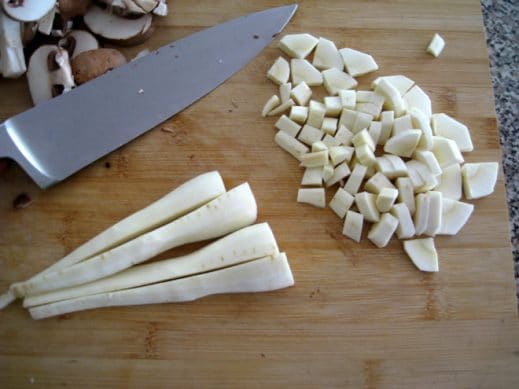 peeled and sliced parsnips on a wood cutting board with a sharp knife