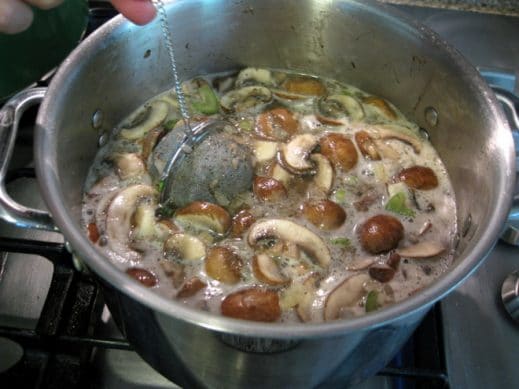 adding a herb ball to a soup pot filled with mushrooms, parsnips, onions, beef and celery