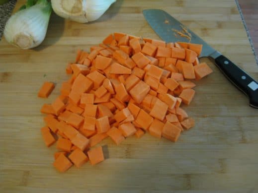 peeled and diced sweet potatoes on a wood cutting board with a sharp knife