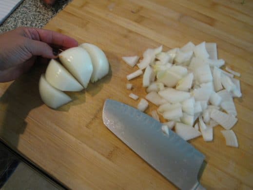half of an onion quartered and a pile of thinly sliced onion on a wood cutting board with a sharp knife