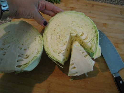 removing the core from a halved green cabbage on a wood cutting board.