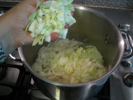 adding chopped cabbage to a soup pot over medium heat