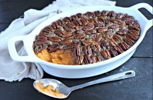 white oval casserole dish filled with healthy sweet potato casserole with pecan topping and a silver serving spoon