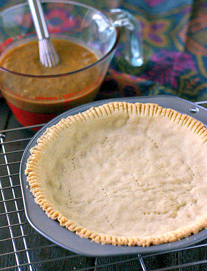 baked paleo pie crust sitting on a wire cooling rack with pumpkin pie filling and linen in the background