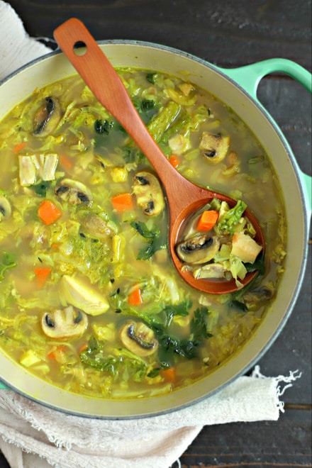 overhead shot of large soup pot with easy turkey soup with cabbage and turmeric with wood ladle and beige linen