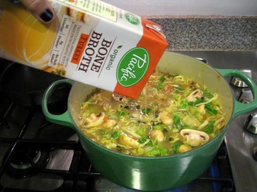 adding turkey bone broth to a large pot of vegetables to make easy turkey soup