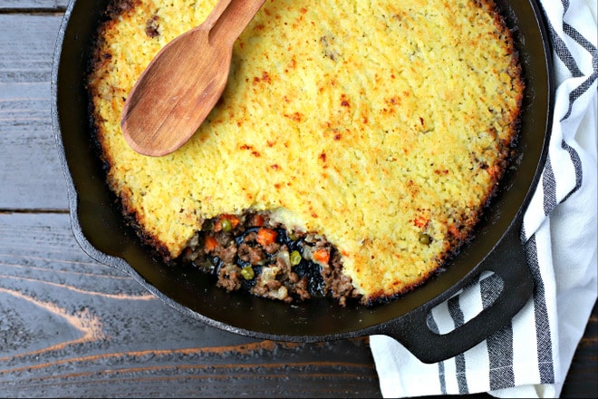 cooked shepherd's pie in a cast iron skillet on top of a black and white striped linen 