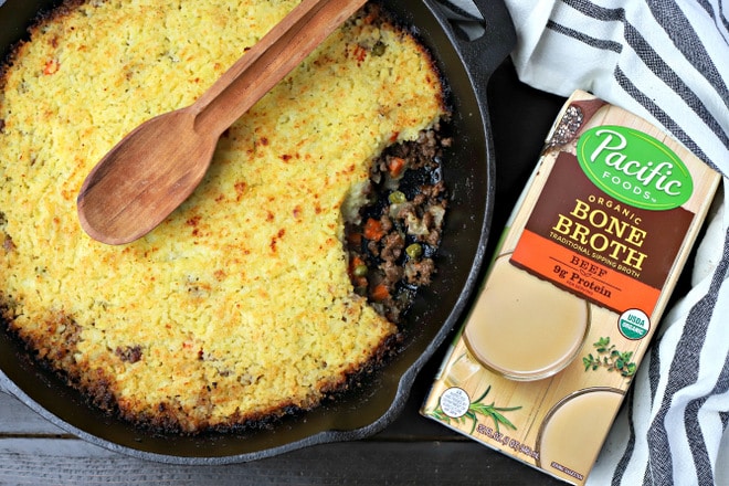 cooked skillet shepherds pie with a wooden spoon on top next to a carton of beef bone broth