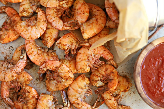 close up overhead shot of cooked old bay shrimp boil topped with extra old bay seasoning with wood bowl filled with cocktail sauce