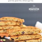 stacks of gluten free biscotti on a beige linen with cranberries and pistachios scattered on the table