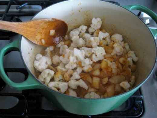 adding cauliflower florets to a soup pot with ingredients to make Garlic Soup