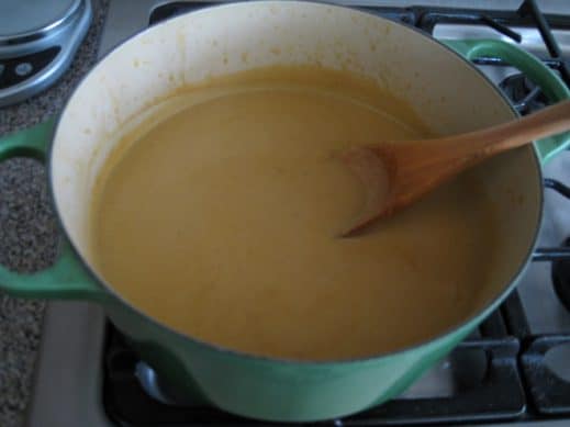 soup pot of creamy pureed Garlic Soup with a wooden spoon sticking out of the pot on the stovetop