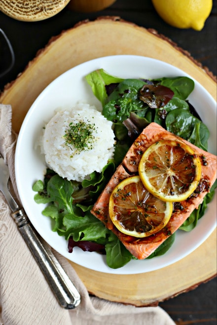 overhead view of white plate with cooked salmon with lemon slices, white rice and salad dressed with balsamic vinaigrette